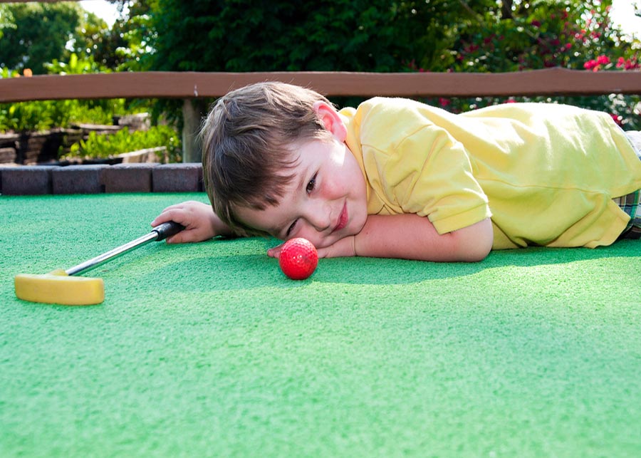 Young boy plays mini golf on putt putt course.